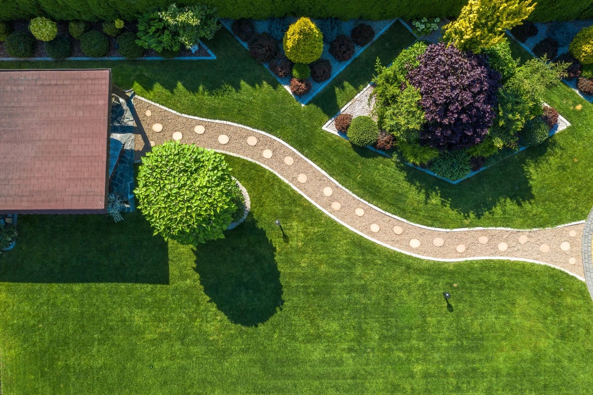Aerial view of a vibrant garden featuring a winding stone path, ornamental shrubs, and well-manicured grass under bright sunlight